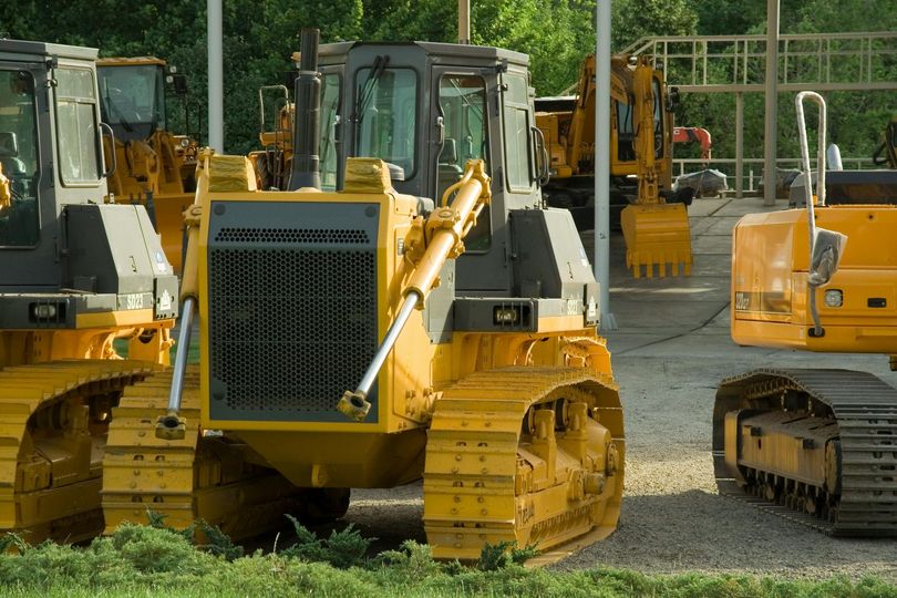 Yellow bulldozers parked in a row on a gravel construction lot on a sunny day.