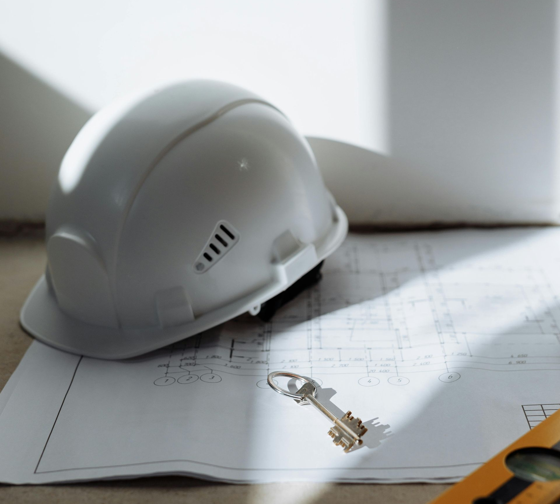 A white hard hat and a metal key resting on architectural blueprints.
