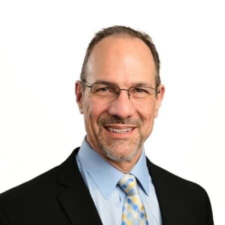 A smiling doctor in a lab coat with a stethoscope around his neck.