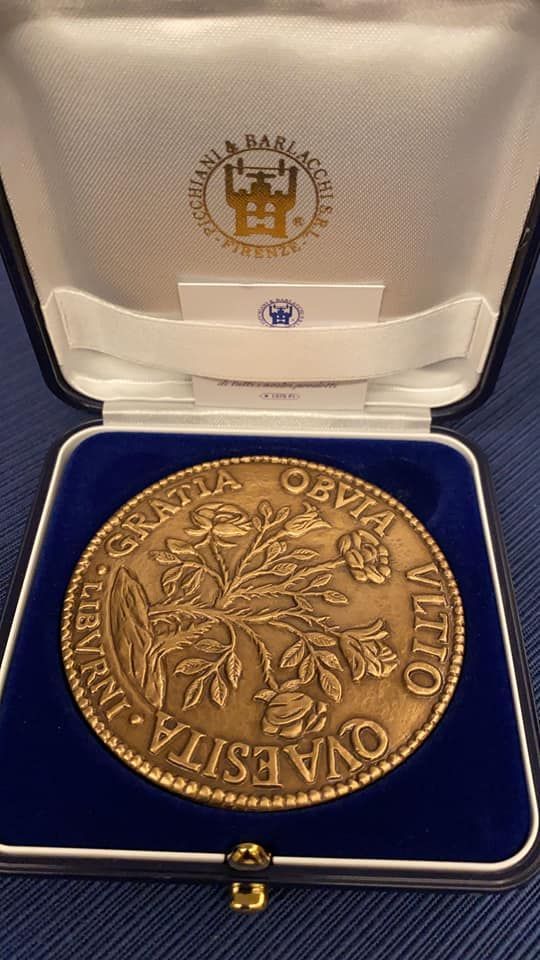 Medaglia di bronzo in una scatola blu con iscrizione e disegno floreale.