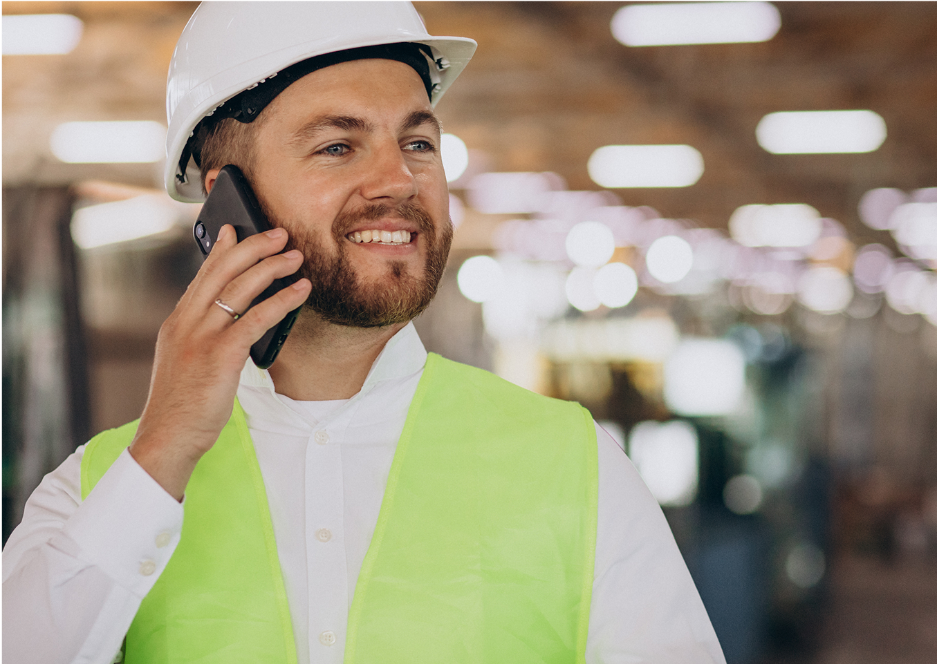 A man wearing a hard hat and safety vest is talking on a cell phone.