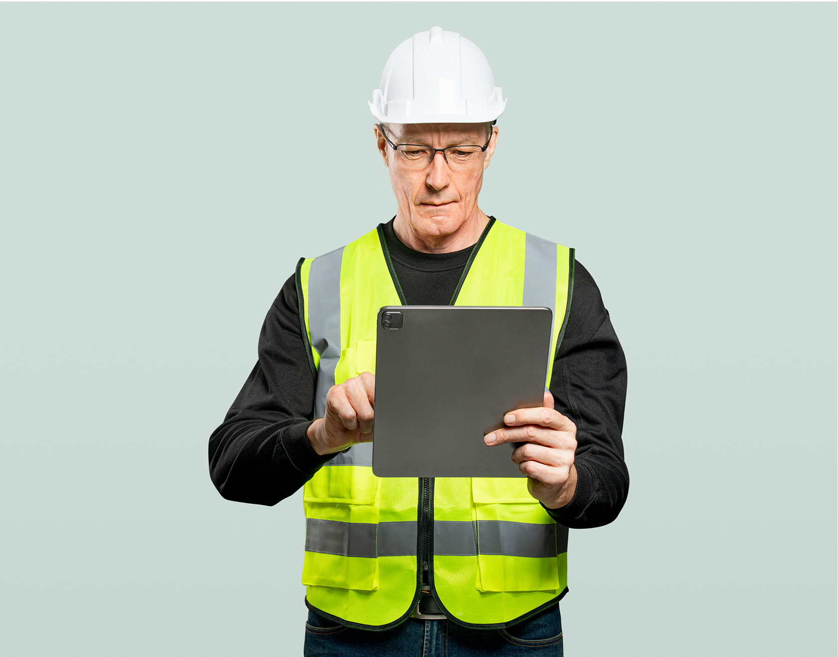 A man wearing a hard hat and safety vest is using a tablet computer.