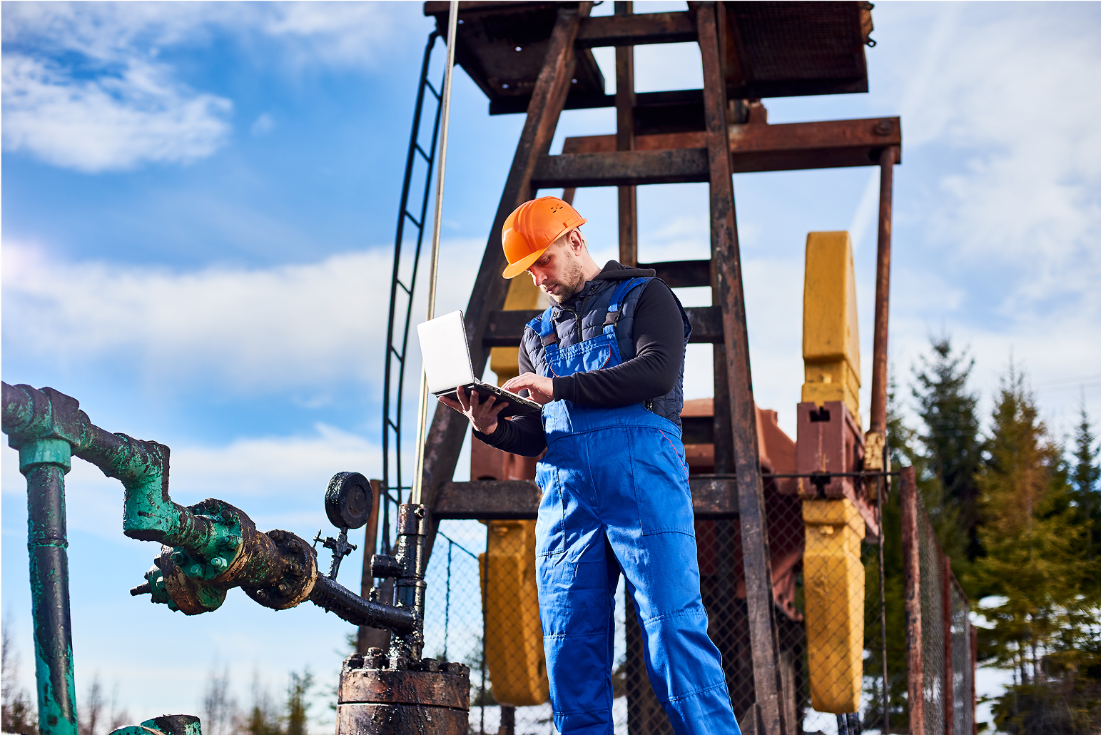 A man is standing in front of an oil pump looking at a tablet.