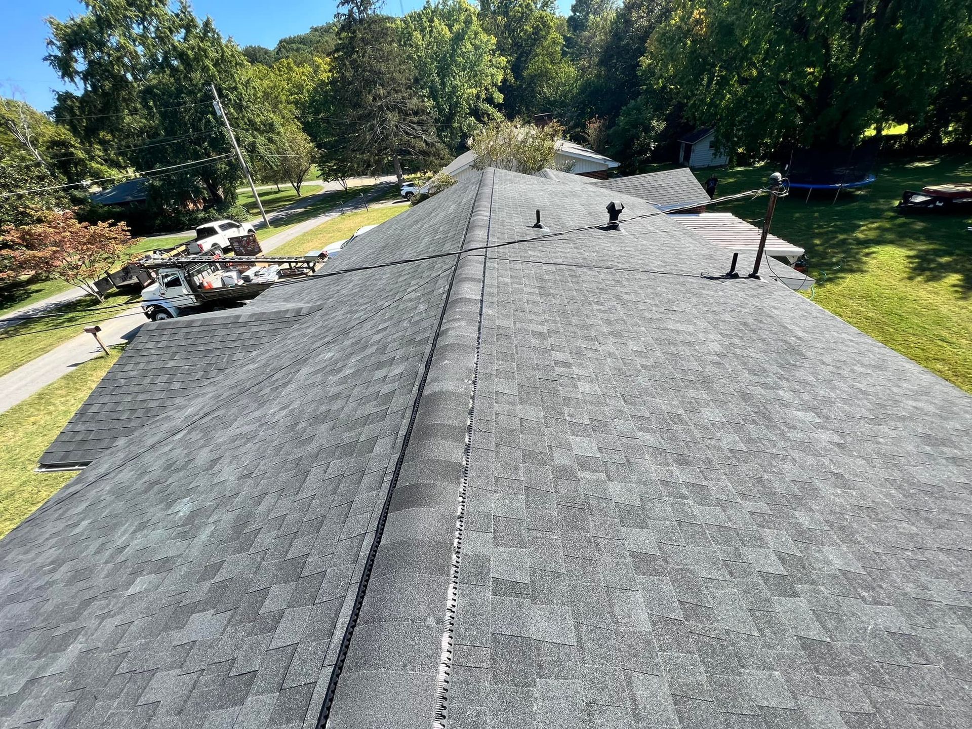 A close-up view of a dark gray shingle roof under a sunny sky.