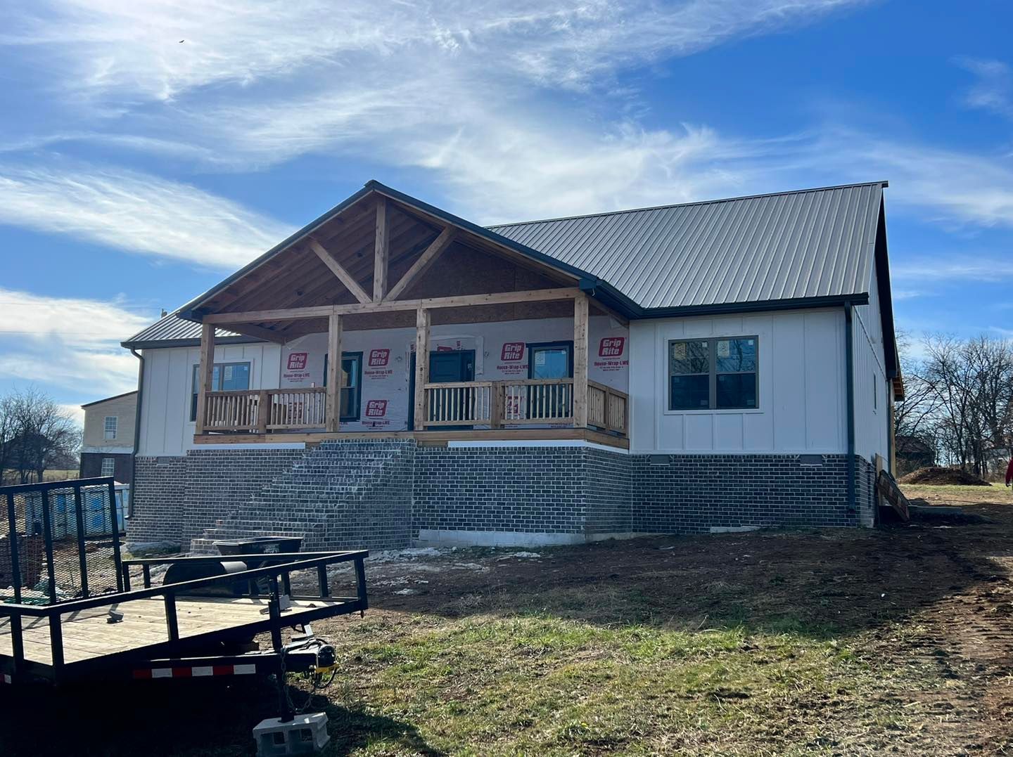House under construction with porch, gray roof, white siding, and brick foundation.