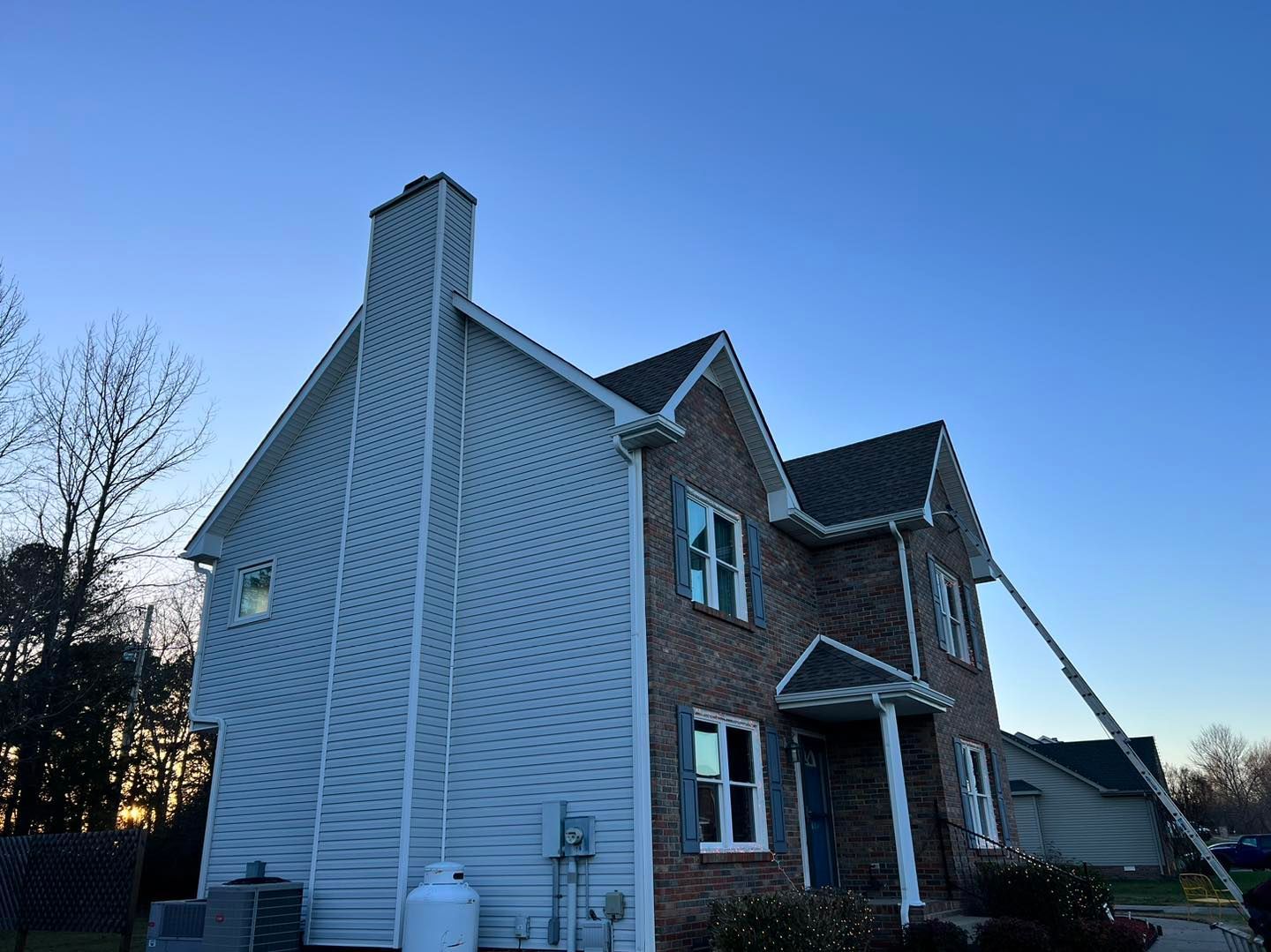 Two-story brick house with white siding and a chimney against a blue sky.