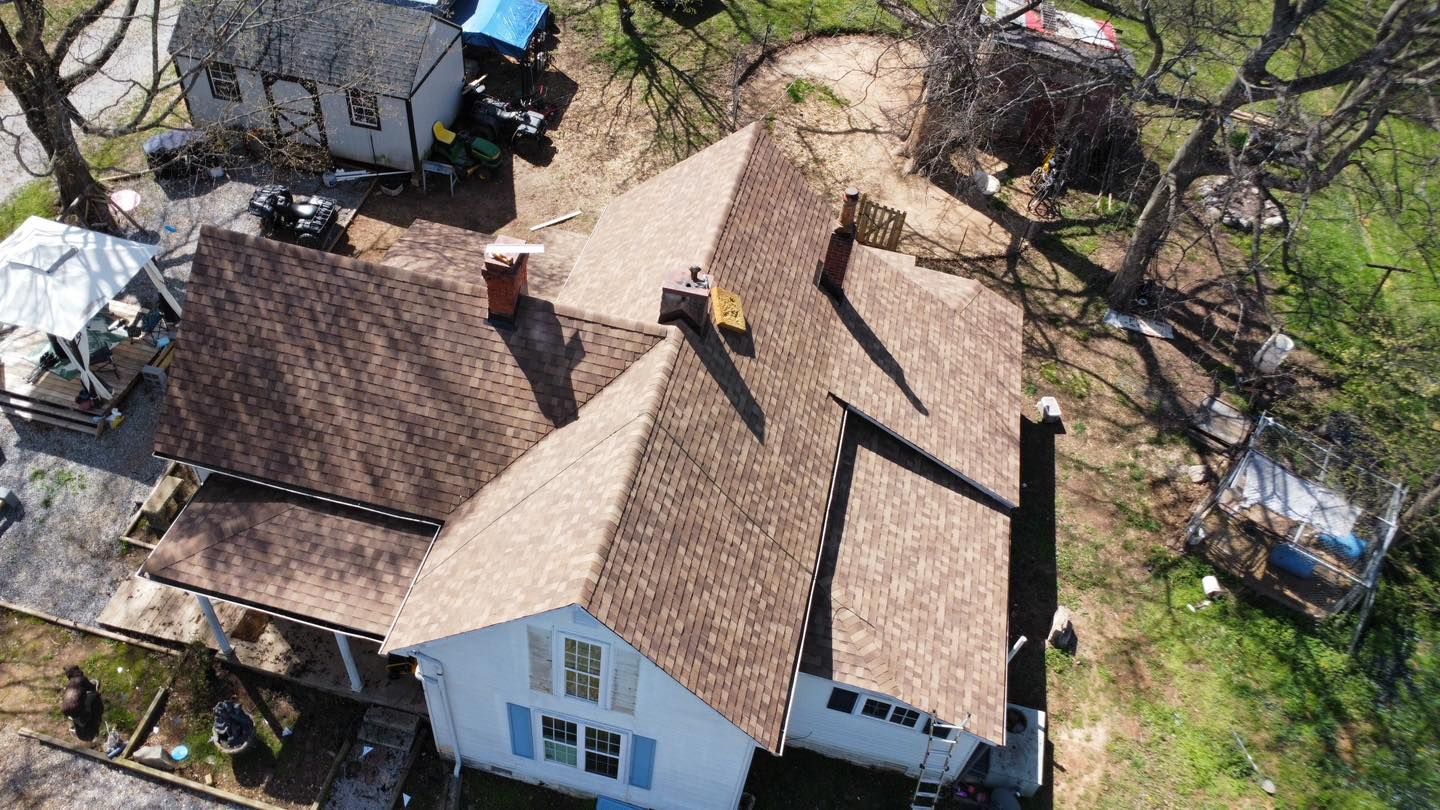 Overhead view of a white house with a brown shingled roof, trees, and a shed.