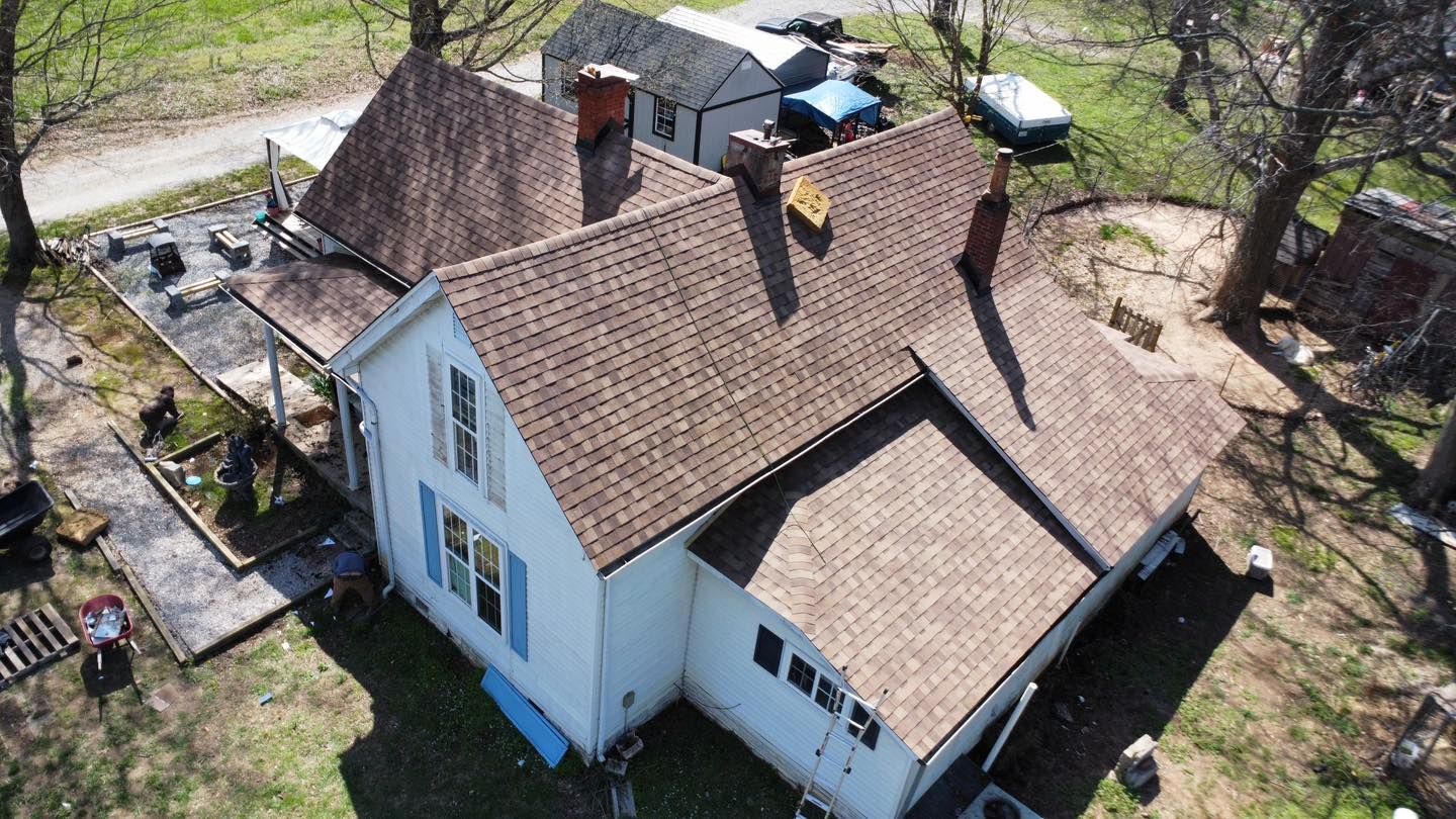 Aerial view of a white house with a brown shingled roof, set in a yard with trees.