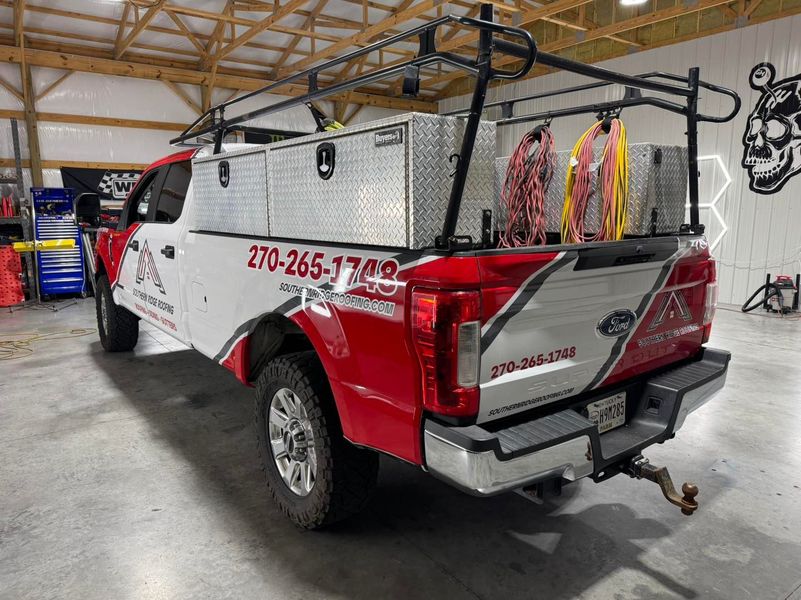 Red and white work truck with storage boxes and a ladder rack, parked inside a garage.