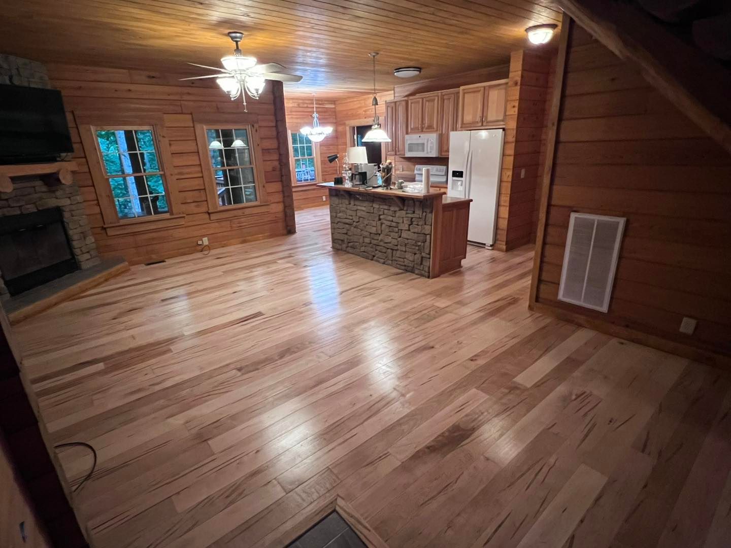 Interior of a wooden cabin with light-colored hardwood floors, kitchen and stone fireplace.