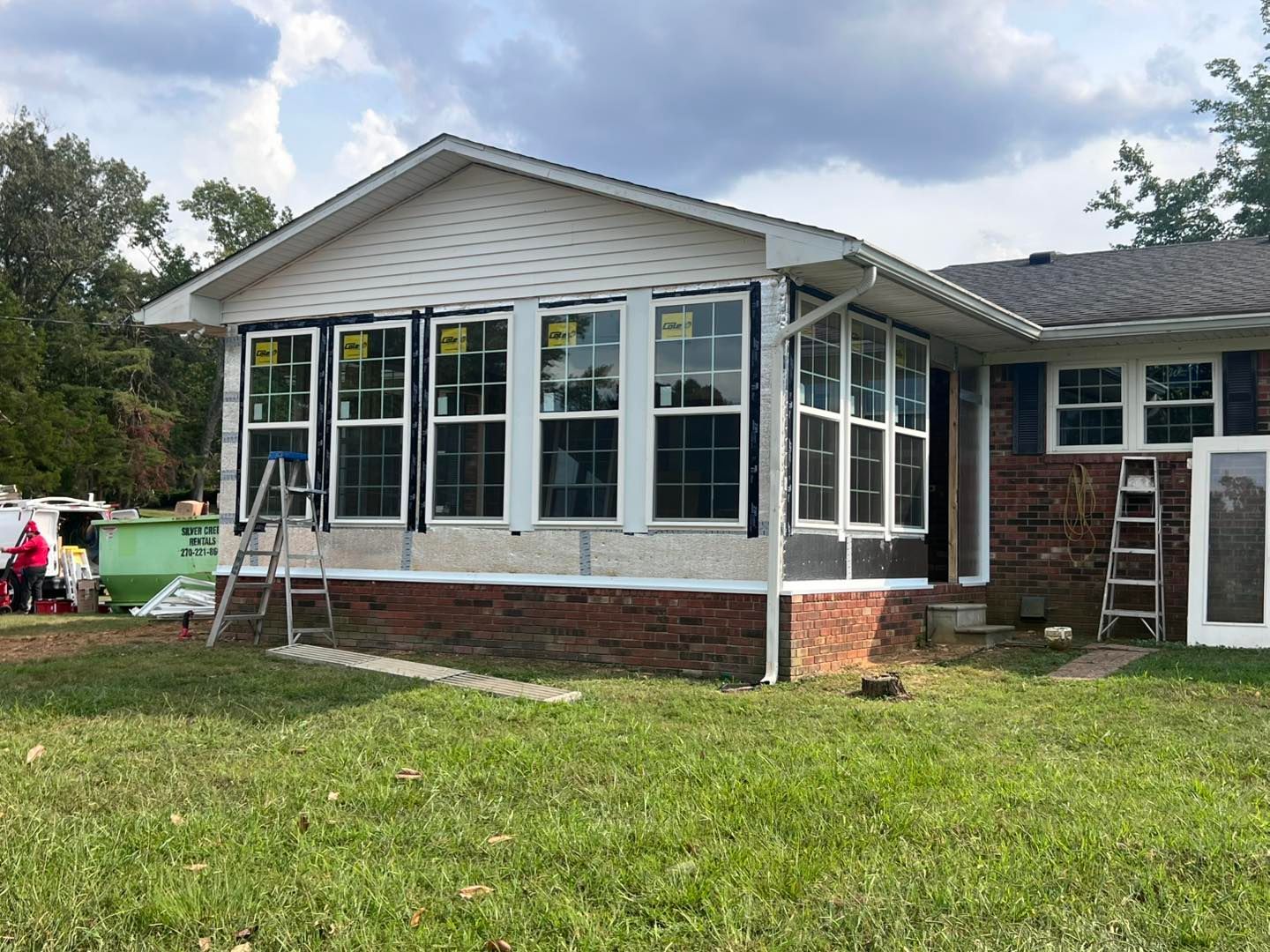 Home with a sunroom addition in progress, visible windows, brick base, and yard.