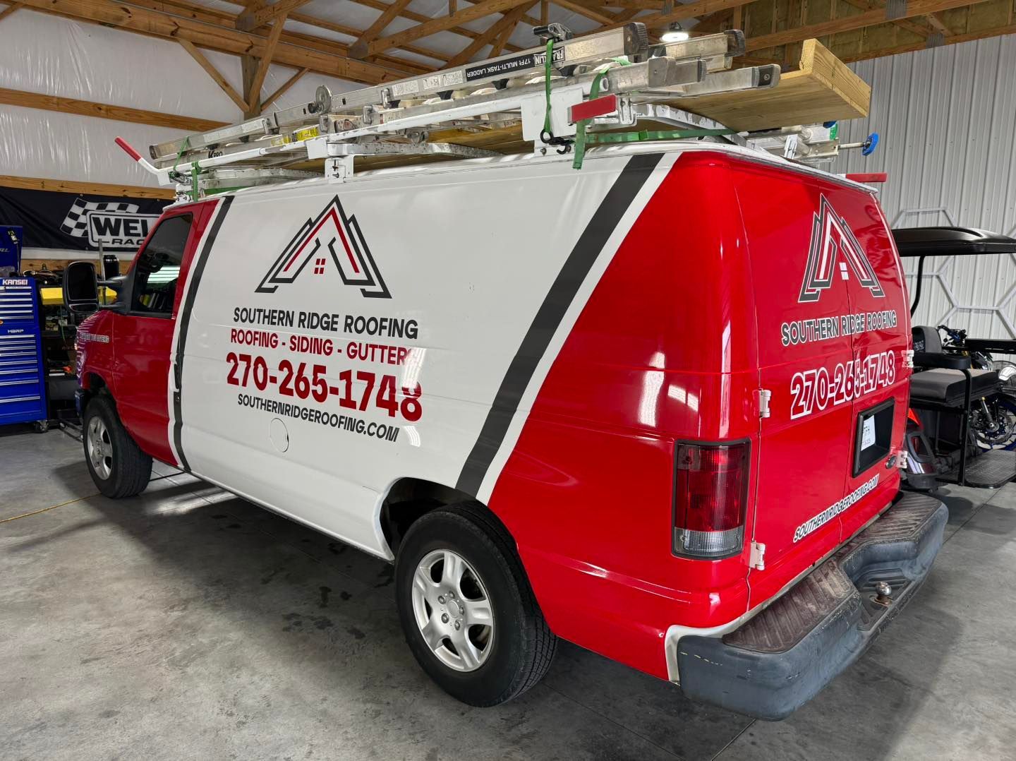 Red and white Southern Ridge Roofing van with ladder on top parked inside a garage.