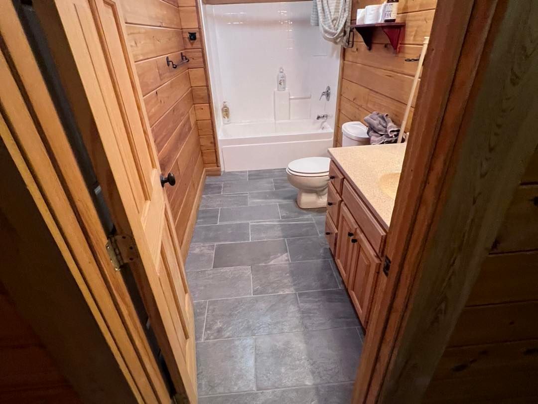 Bathroom with wooden walls, blue-gray tile floor, toilet, vanity, and shower/tub.