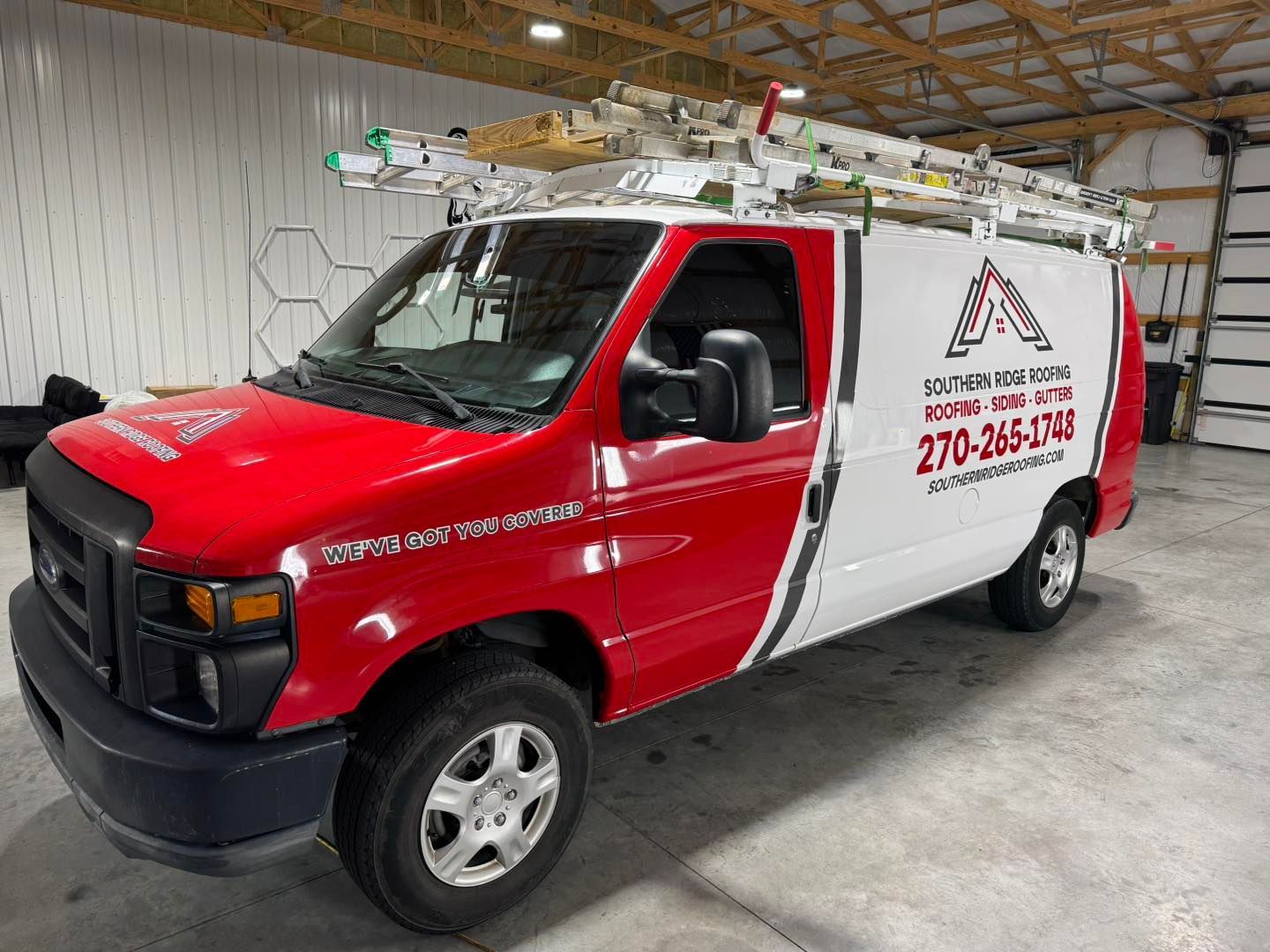 Red and white work van with ladders on top; company logo and phone number on the side.