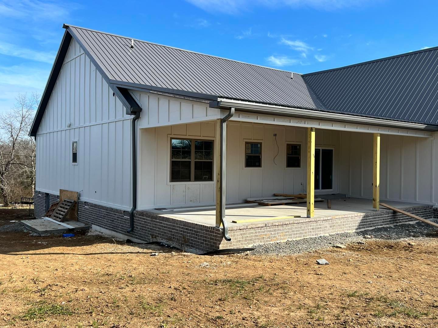 Newly constructed house with white siding, metal roof, and covered porch on a sunny day.