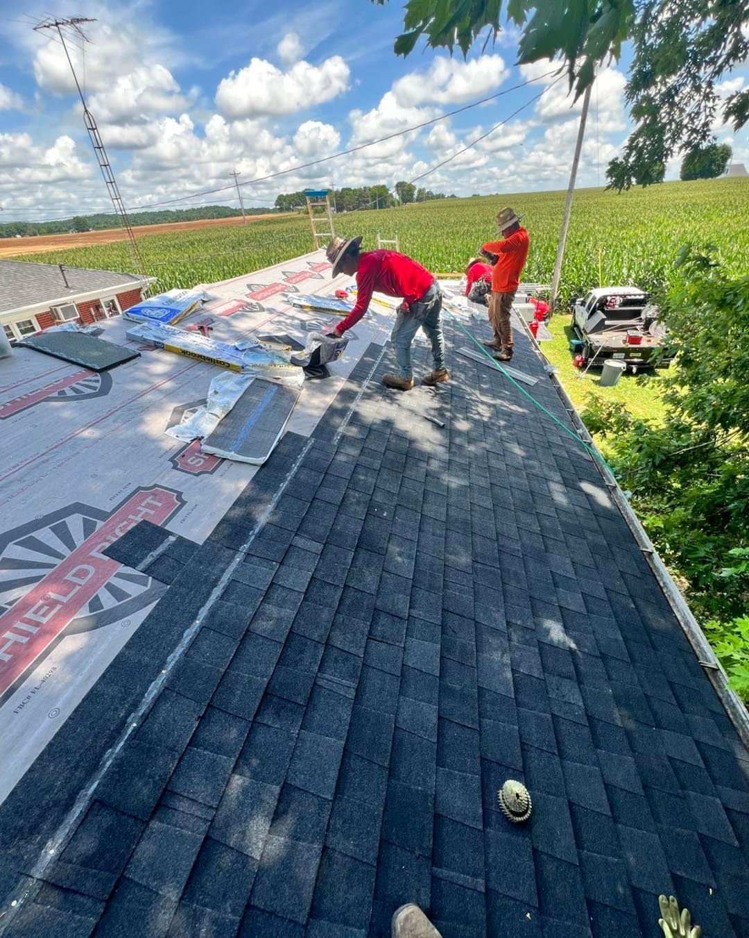 Two workers installing roofing shingles on a residential house on a sunny day.