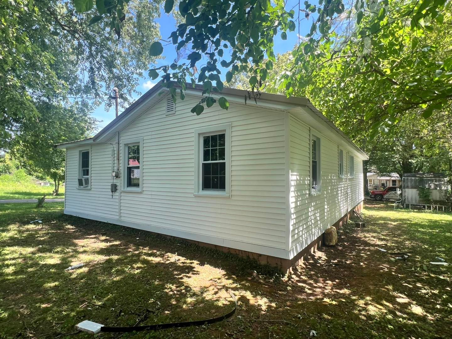 White house with several windows, surrounded by green trees and grass, on a sunny day.
