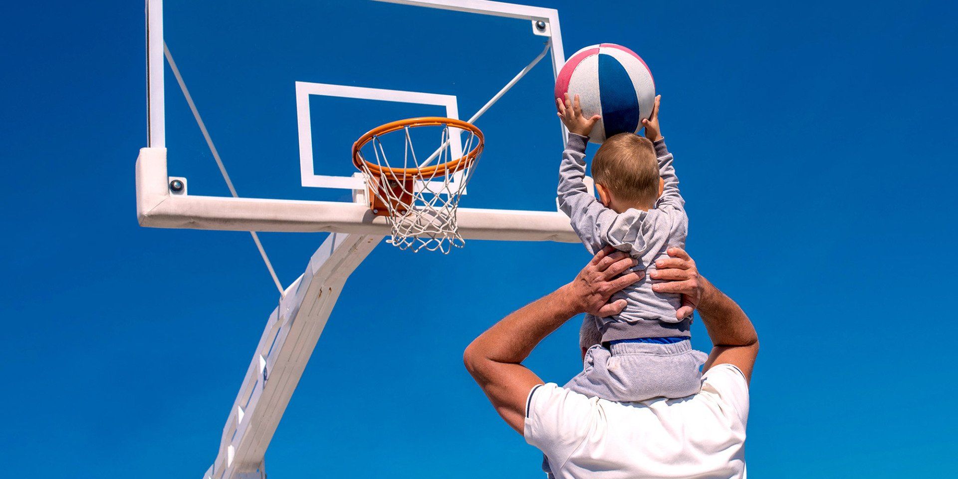 dad lifts son on his shoulders to dunk a basketball