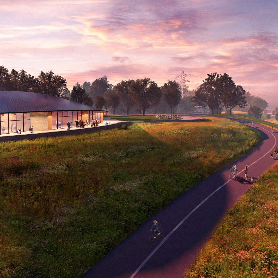 Building with glass walls, curving paved path with people biking, grassy field, and trees at sunset.