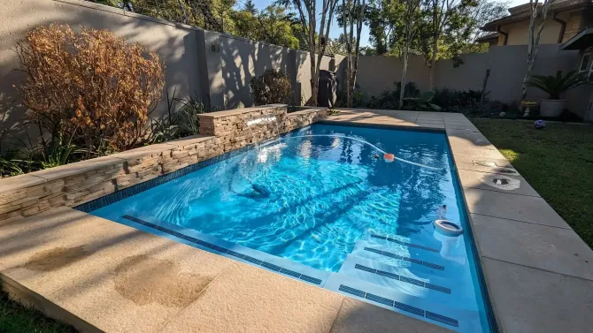 Blue-tiled rectangular pool with steps in a backyard. Light-colored patio surrounds the pool.