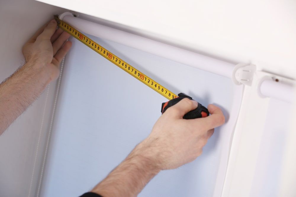 A Person Is Measuring A Blind With A Tape Measure — Budget Home Improvements In Kingscliff, NSW