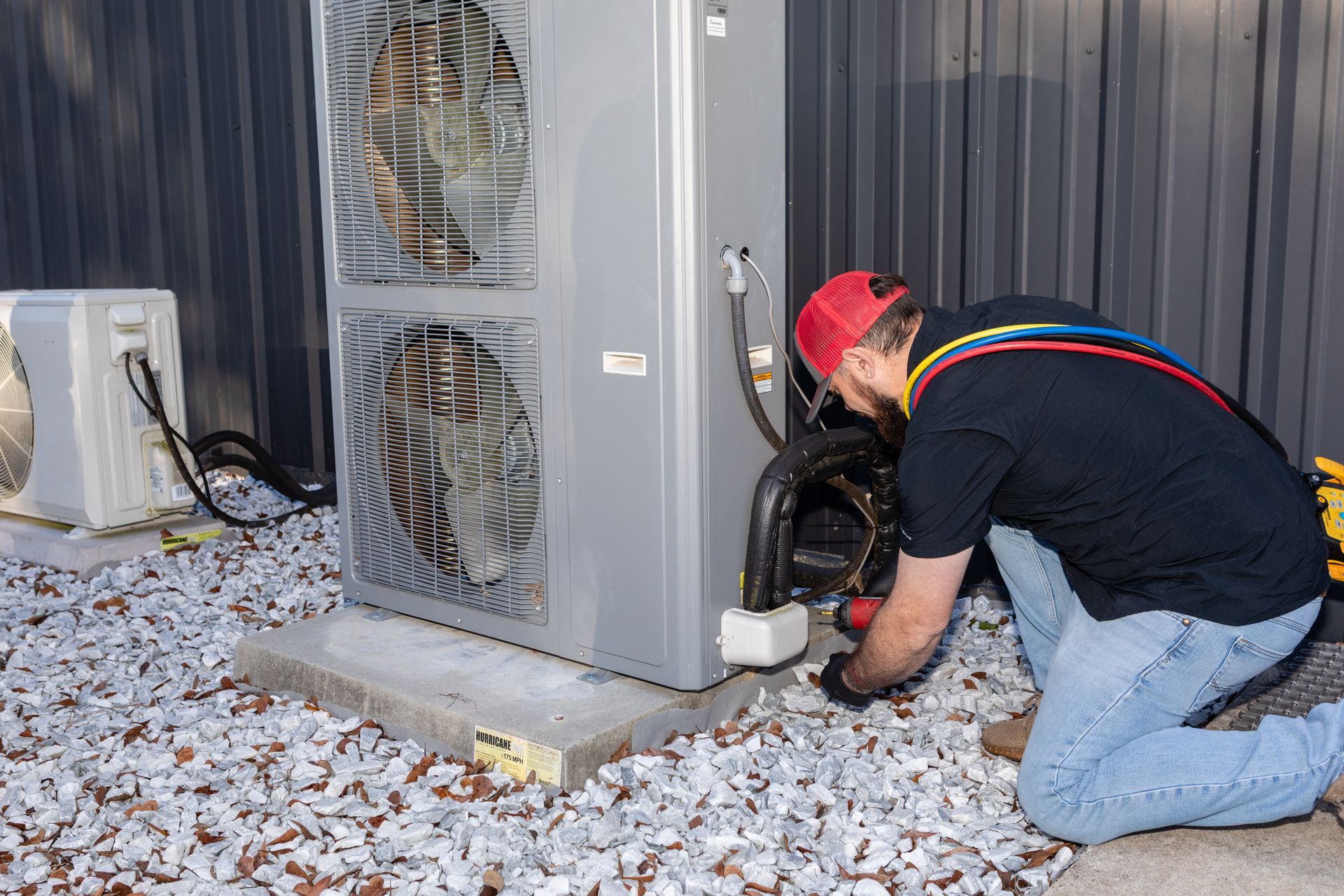 Outdoor air conditioning unit mounted on a brick wall, near a garden with shrubbery.