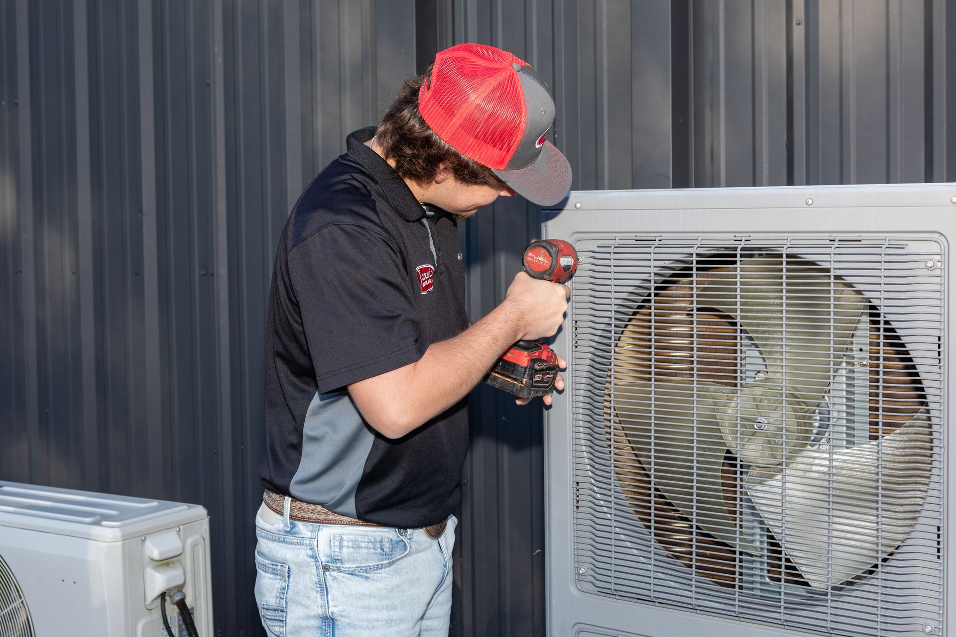 Person in a cap and gloves fixing a white air conditioning unit with a screwdriver.