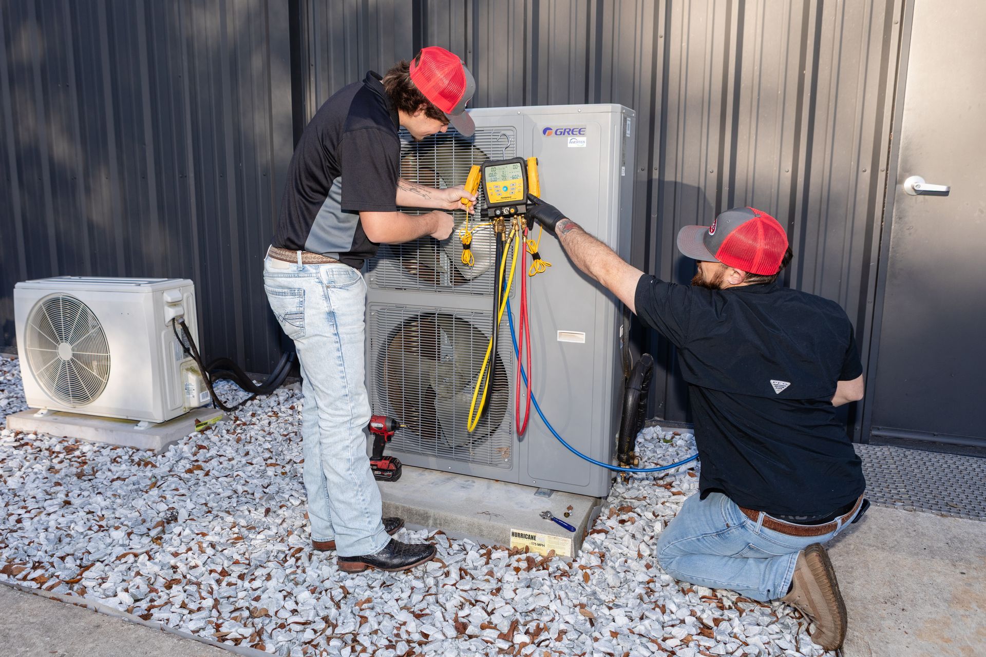 Two outdoor air conditioning units near a brick wall, sitting on concrete pads.