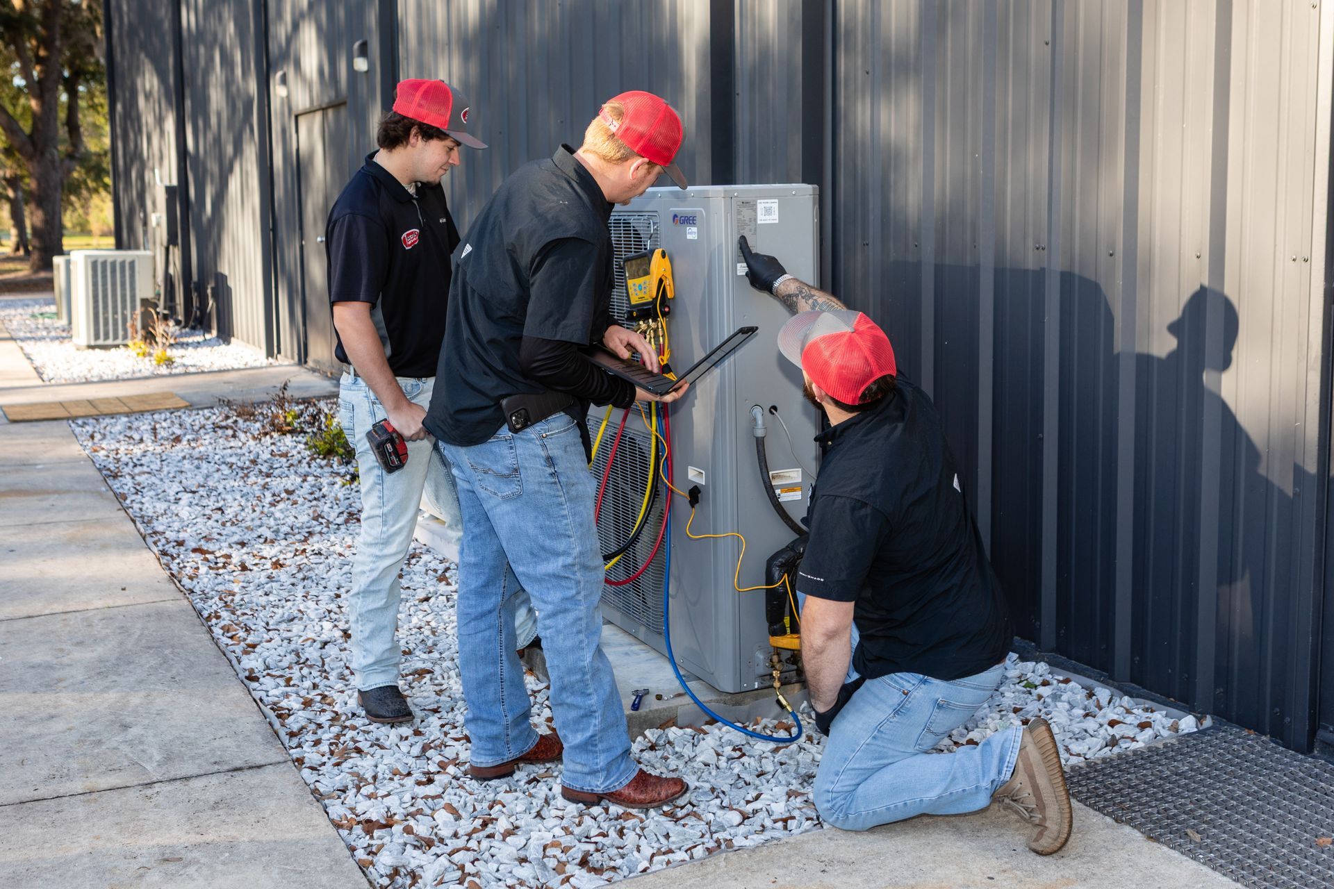 Two outdoor air conditioning units next to a wooden wall and green grass.
