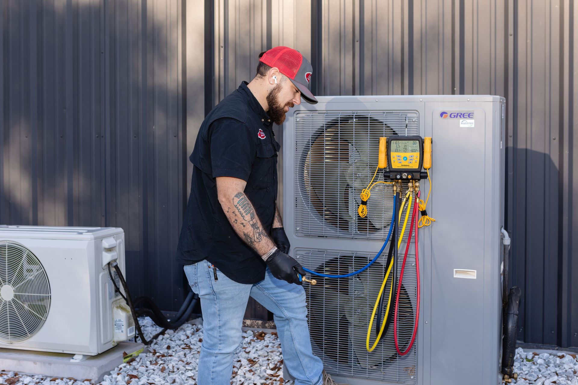 HVAC technician in blue jumpsuit, inspecting an outdoor AC unit; outdoors, sunlight.