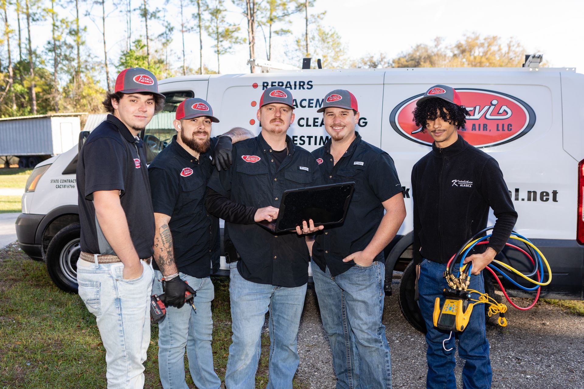 Two air conditioning units in a yard, near greenery and a brick wall.