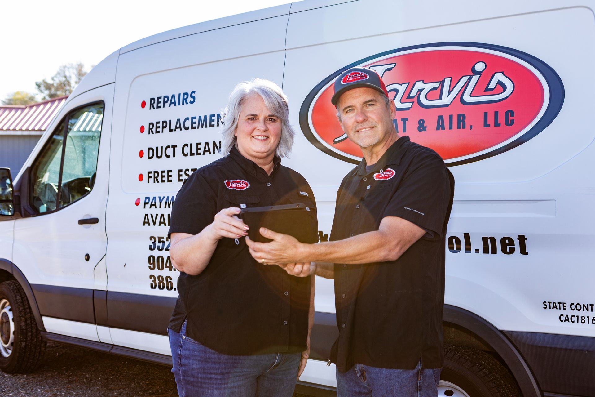 Hand holding a remote control pointing towards a mounted white air conditioner unit. Room interior.