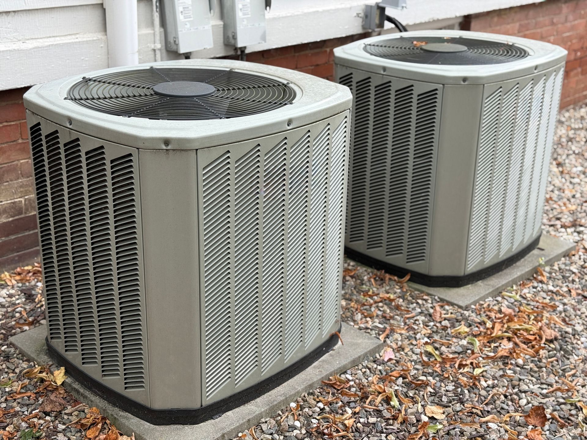 Two gray air conditioning units sitting on concrete pads outside a building.