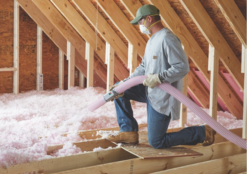 Person installing insulation in an attic, using a hose to dispense the fluffy material.