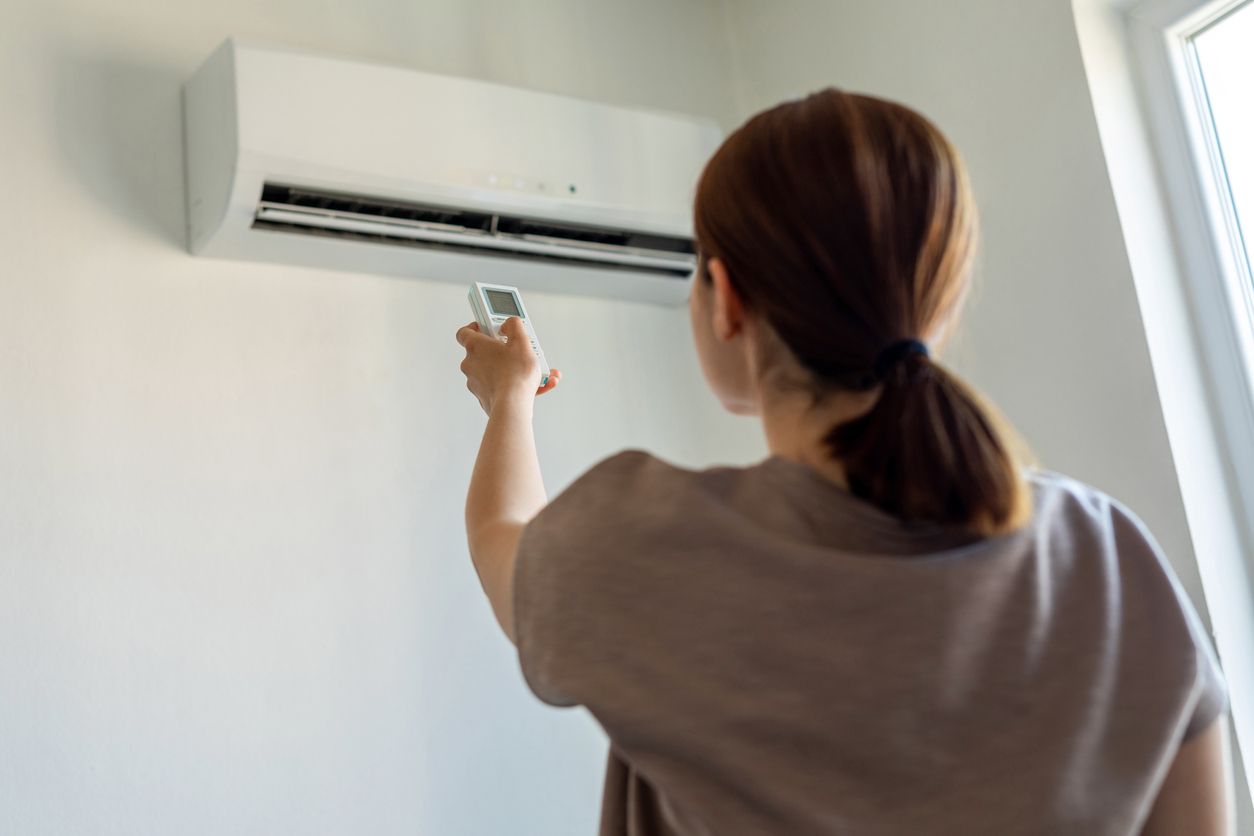 Woman using a remote to control a wall-mounted air conditioner.