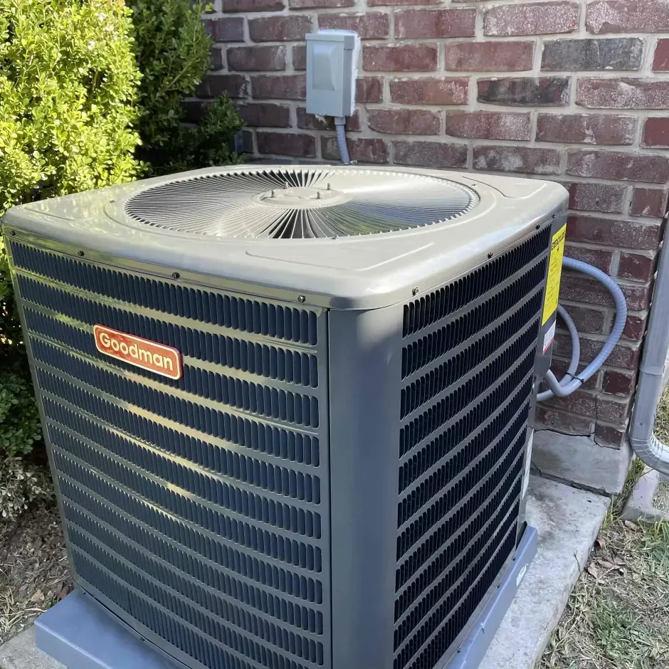 Two outdoor air conditioning units next to a wooden wall and green grass.