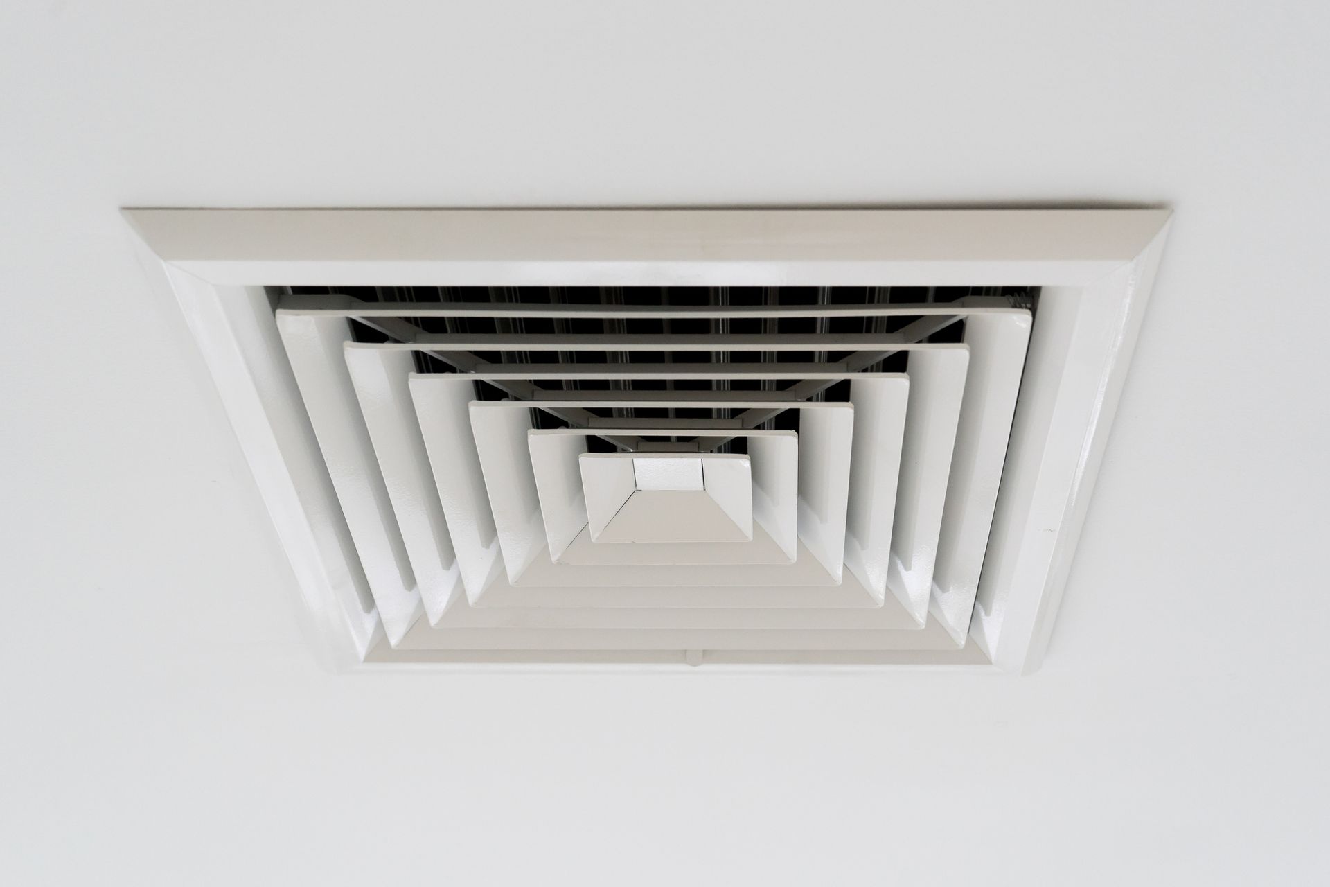 Man working on an air duct above an air conditioner. Gray walls, silver ductwork.