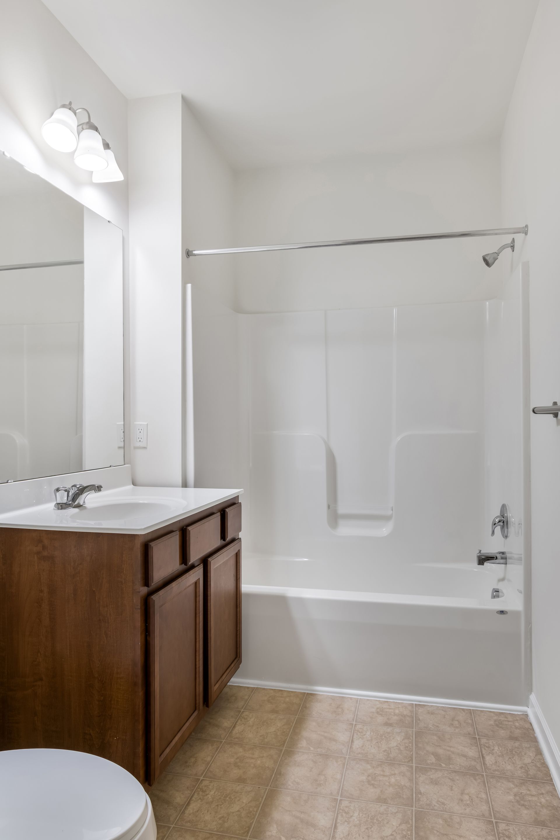 A bathroom featuring a wooden vanity, a white countertop with a sink, a mirror, and a white bathtub-shower combination.