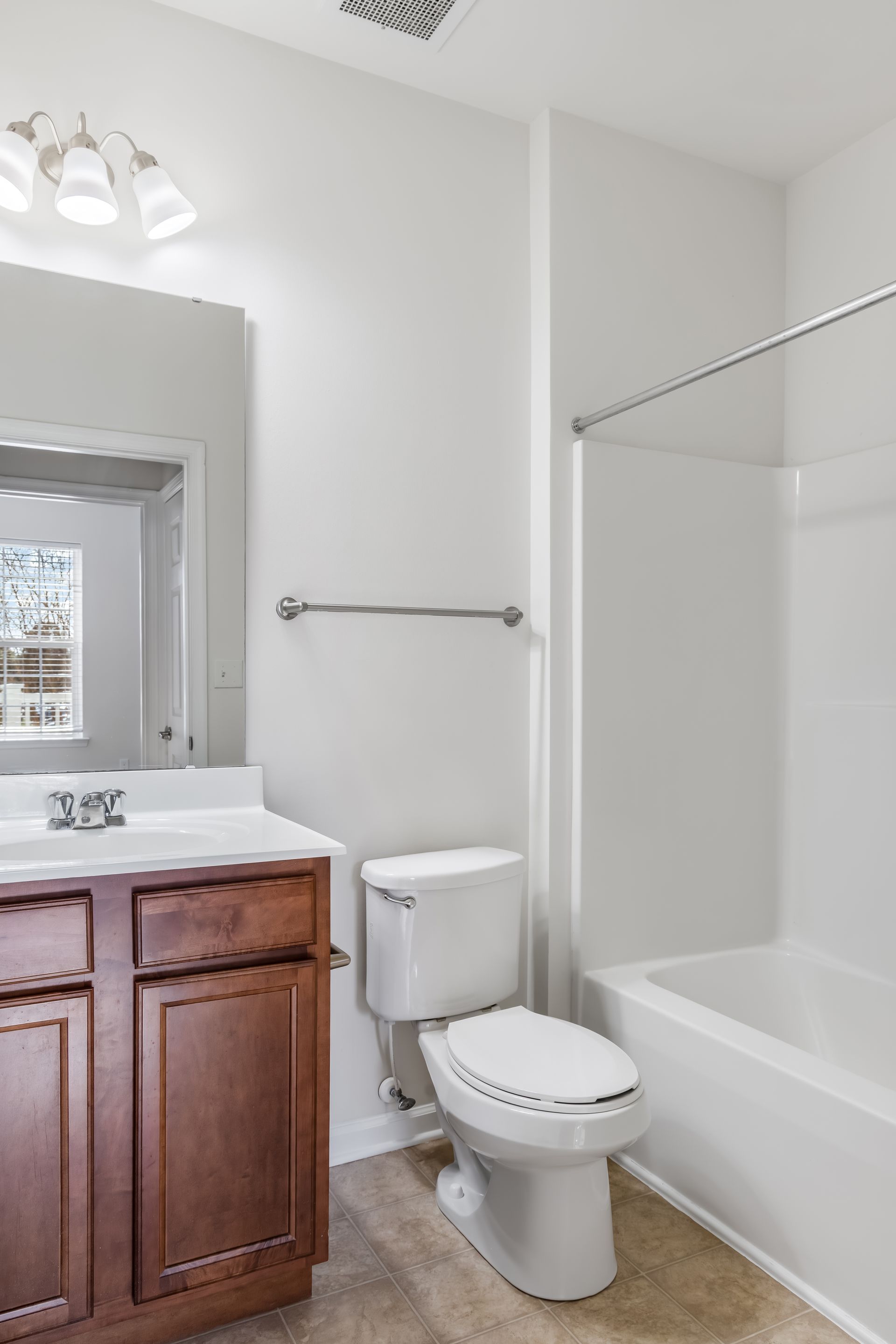 A small bathroom with a wooden vanity, white sink, toilet, and a bathtub with a shower rod against white walls.