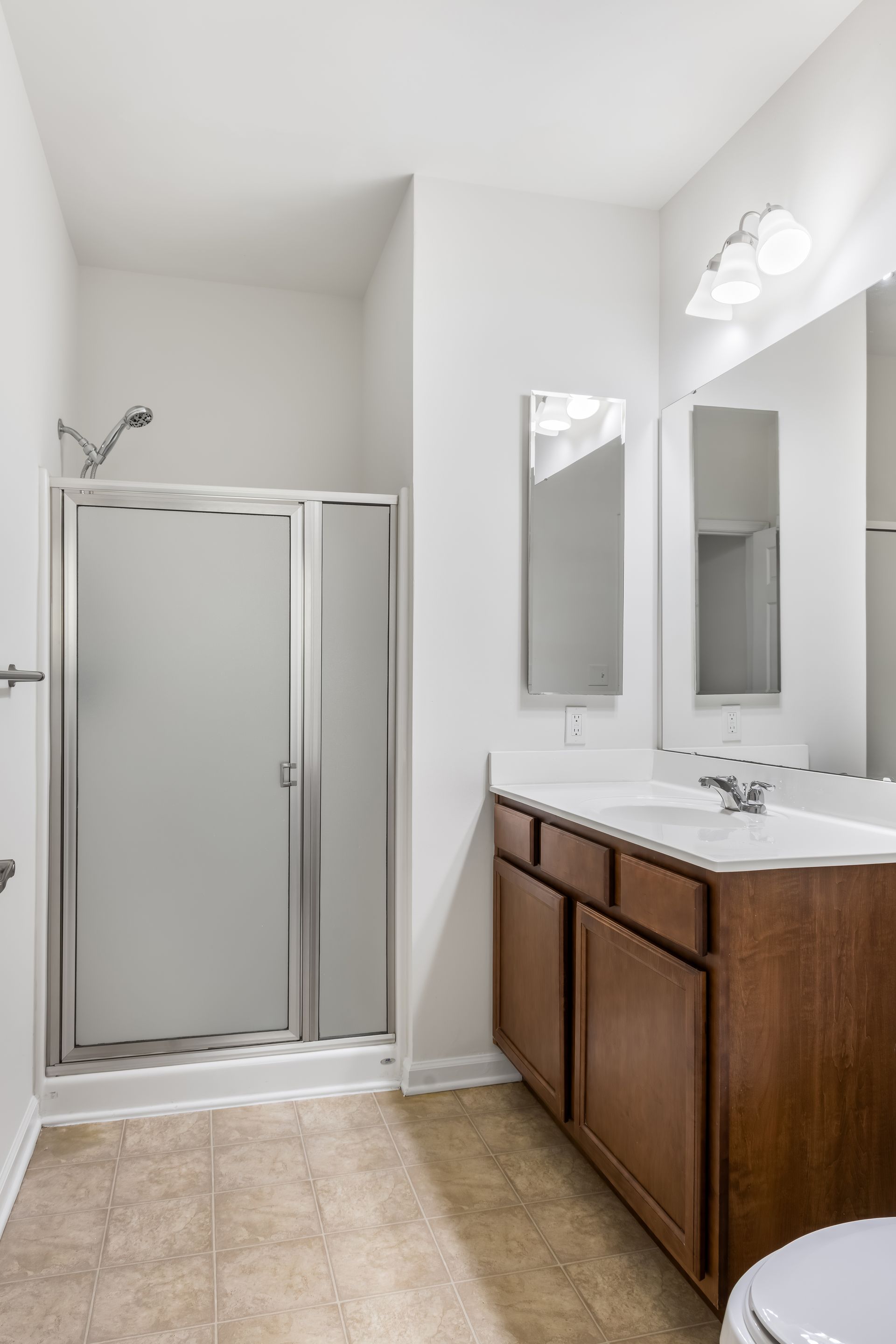 A modern bathroom featuring a walk-in shower with a silver frame, a wooden vanity with a white countertop, and a mirror.