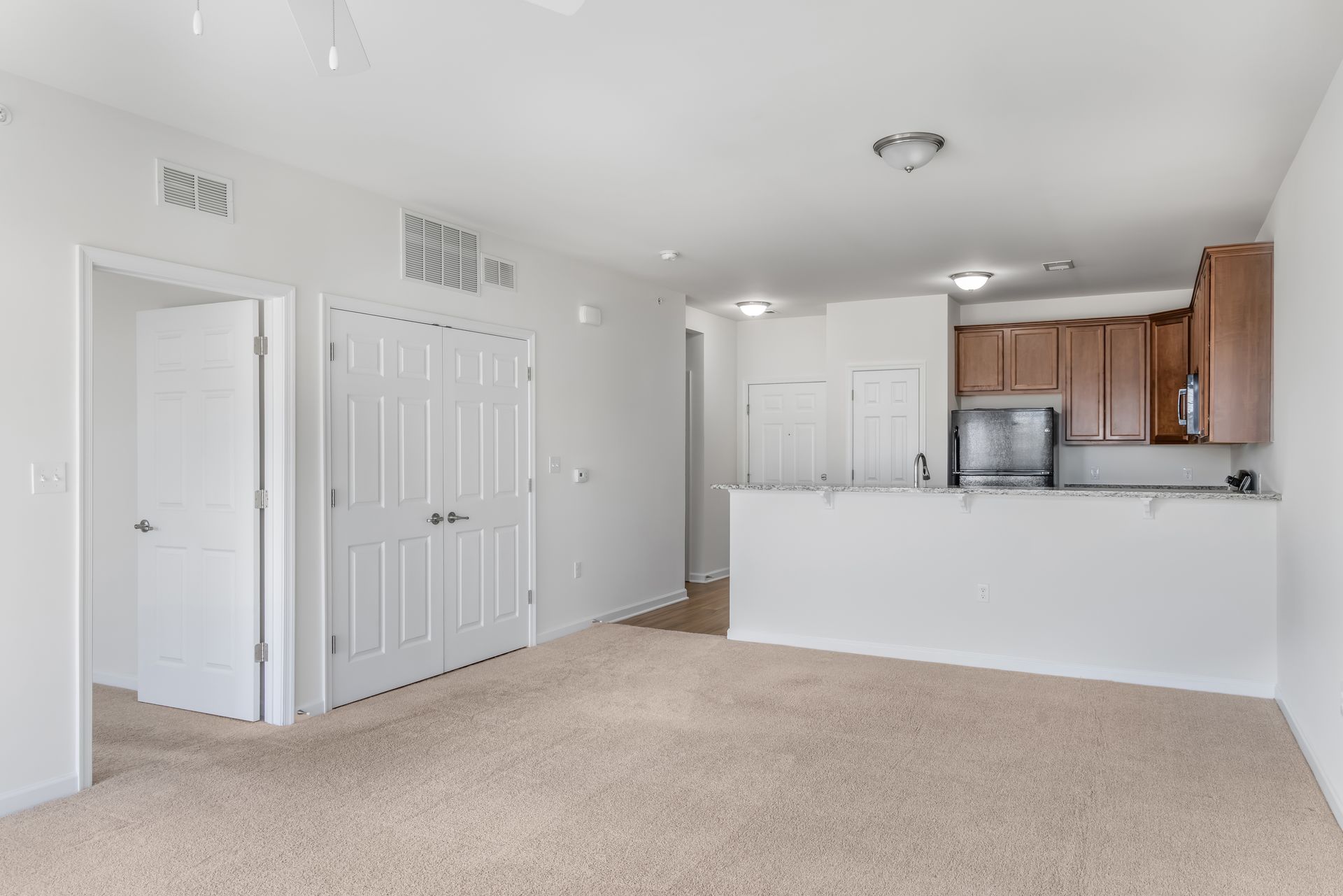 A neutral-toned room with beige carpet, white walls, double closet doors, an open doorway, and a kitchen island bar.