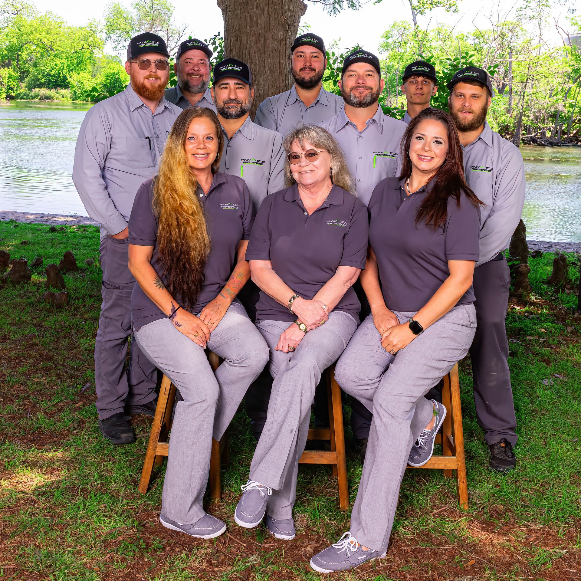 Group of people in matching grey uniforms posing outside near a body of water.