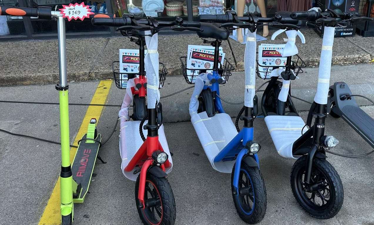 Row of electric scooters in various colors, for sale outside a store.