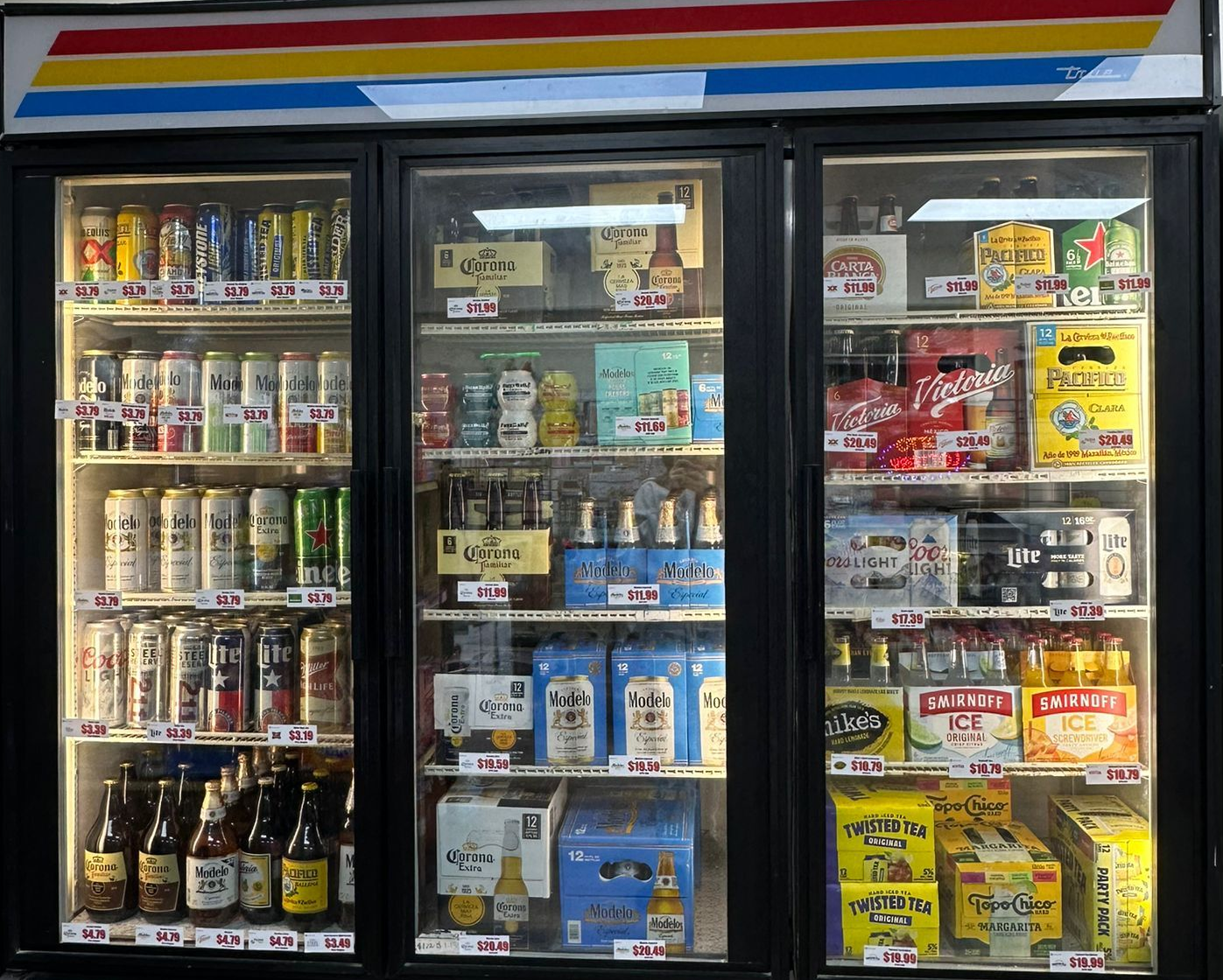 Three-door refrigerated display case stocked with various beers and beverages in a convenience store.