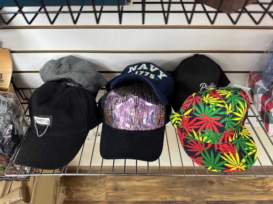 Hats on a shelf: black, navy, green marijuana leaf, and grey, in a store setting.