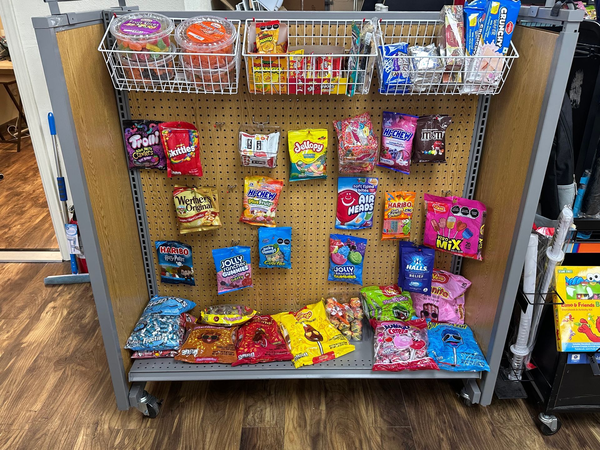 Candy display cart with shelves and pegboard, filled with colorful packaged candies.