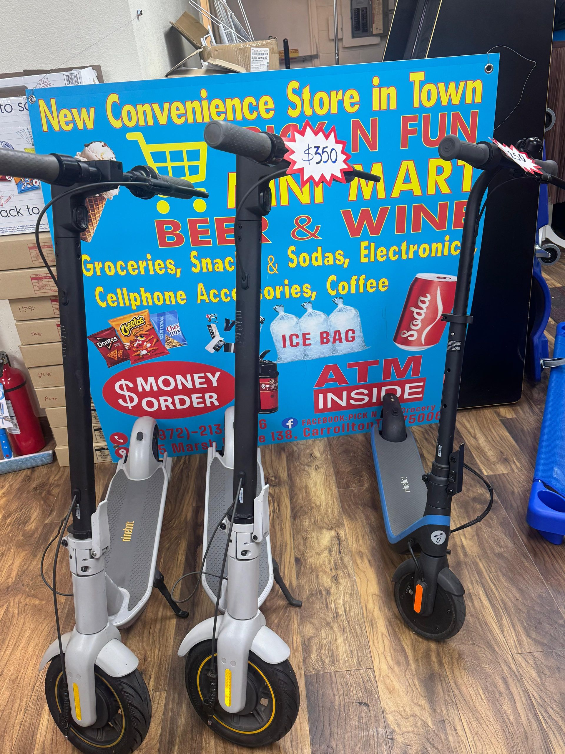 Three electric scooters in a convenience store, with store sign in the background.