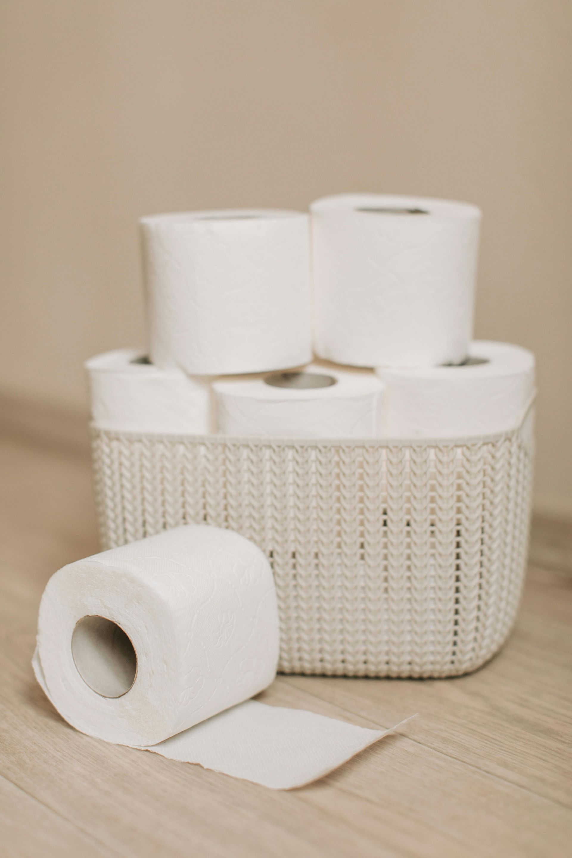 White toilet paper rolls in a wicker basket on a light wooden floor.