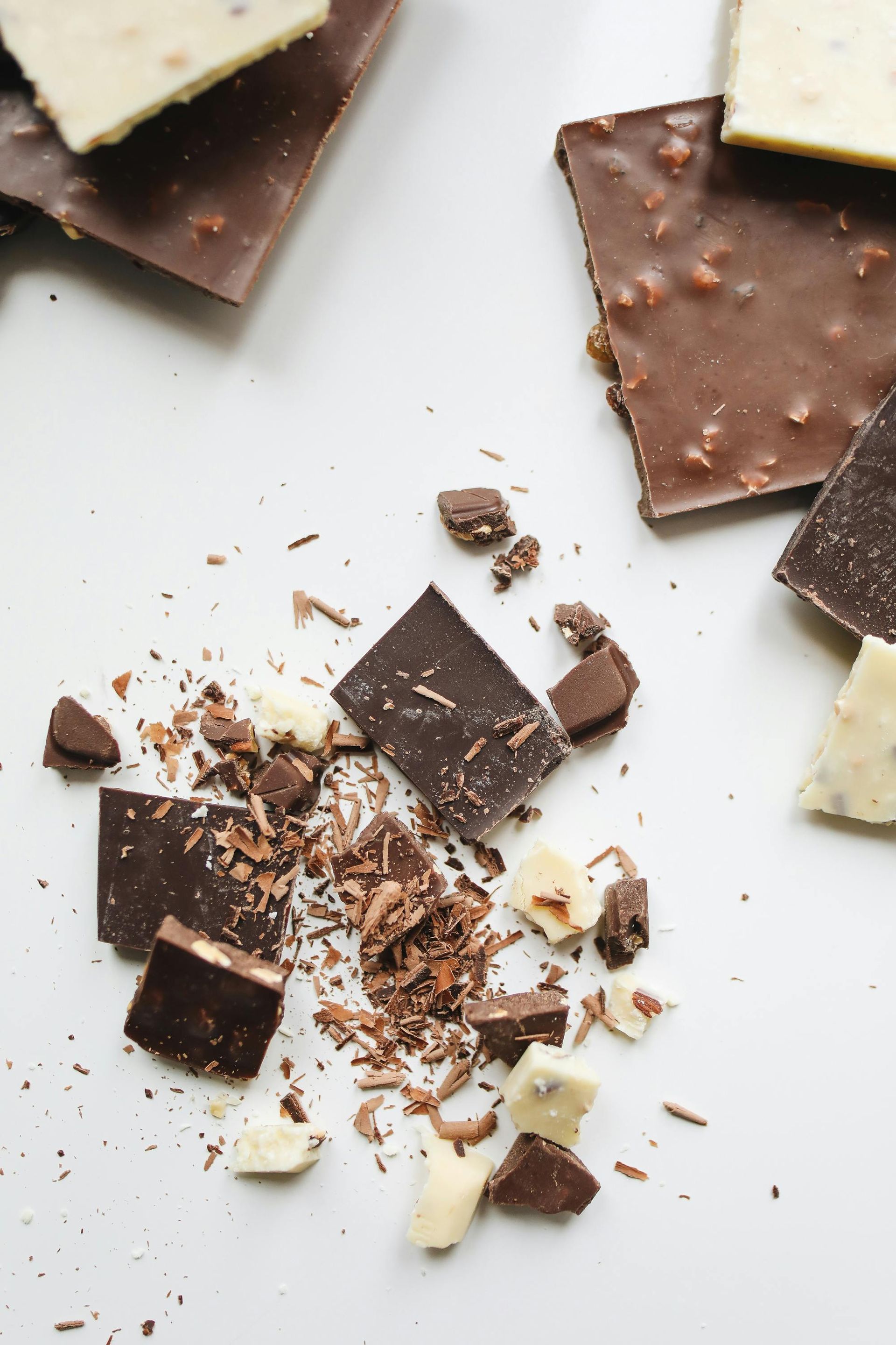 Broken squares of dark and white chocolate with shavings, scattered on a white surface.