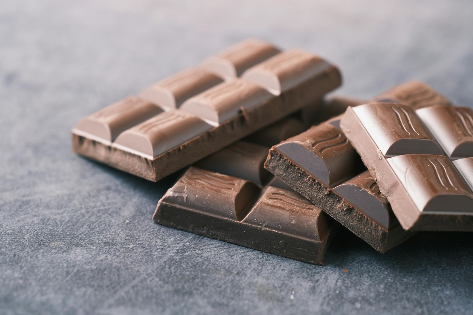 Several pieces of milk chocolate on a gray surface.